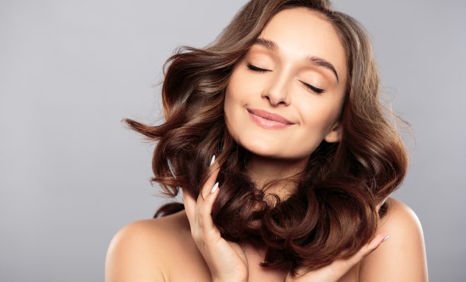 Brunette girl with healthy curly hair and natural make up . Beautiful model woman with wavy hairstyle .Care and beauty